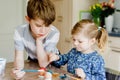 Excited little toddler girl and older brother, school kid boy coloring eggs for Easter. Two cute children, siblings Royalty Free Stock Photo