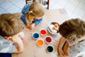 Excited little toddler girl and two kids boys coloring eggs for Easter. Three children, siblings looking surprised at Royalty Free Stock Photo