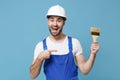 Excited man in coveralls protective helmet hardhat pointing index finger on paint brush isolated on blue wall background Royalty Free Stock Photo