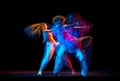 Excited man and woman dancing hip-hop in sportive style clothes on dark background at dance hall in mixed neon light Royalty Free Stock Photo