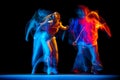 Excited man and woman dancing hip-hop in sportive style clothes on dark background at dance hall in mixed neon light Royalty Free Stock Photo