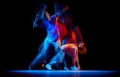 Excited man and woman dancing hip-hop in sportive style clothes on dark background at dance hall in mixed neon light Royalty Free Stock Photo