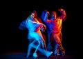 Excited man and woman dancing hip-hop in sportive style clothes on dark background at dance hall in mixed neon light Royalty Free Stock Photo