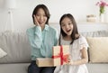Excited mature Asian woman and her adorable little granddaughter opening gift on couch at home Royalty Free Stock Photo