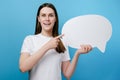 Excited millennial young woman holding and pointing at blank speech bubble, dressed in white t-shirt Royalty Free Stock Photo