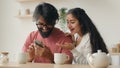 Excited multiethnic family Arabian indian man and woman looking at mobile phone screen at home kitchen happy couple girl Royalty Free Stock Photo