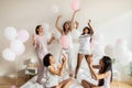 Excited multiracial girls throwing balloons in air at pajamas party.