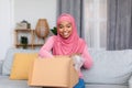 Excited muslim woman opening cardboard box, receiving online store order, satisfied with good delivery service Royalty Free Stock Photo