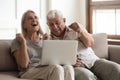 Excited older wife and husband celebrating online win, using laptop