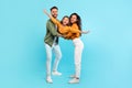 Excited parents playing with daughter holding her in arms posing on blue background, girl spreading hands like plane