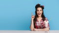 Excited pinup woman in retro clothes sitting at table with milk shake, gesturing eureka over blue background, copy space