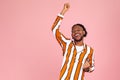 Excited positive bearded afro-american man in stylish eyeglasses and striped shirt dancing, raising hands up and having fun, good