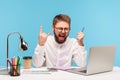 Excited positive man office worker showing rock and roll gesture sitting at workplace with laptop notepad and pencil, successfully