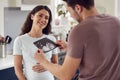 Excited Pregnant Transgender Couple At Home In Kitchen Looking At Ultrasound Scan Of Baby