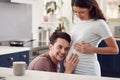 Excited Pregnant Transgender Couple At Home In Kitchen With Man Listening To Baby\'s Heartbeat