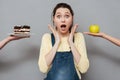 Excited pregnant woman choosing between apple and a cake Royalty Free Stock Photo