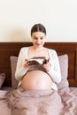 Excited pregnant woman is eating a slice of cake resting in bed at home. Love to sweet during pregnancy Royalty Free Stock Photo