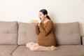Excited pregnant woman is eating a slice of cake resting on the sofa at home. Love to sweet during pregnancy Royalty Free Stock Photo