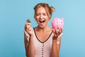 Excited pretty woman with blonde hair and wearing summer dress, yelling happily, holding piggy bank and gold crypto coin, growth