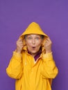 Excited of a rain holding yellow water proof rubbered raincoat hood mature grey haired woman isolated on purple Royalty Free Stock Photo