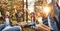 Excited school kids raising arms and screaming while sitting on grass in forest with notebooks