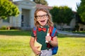 Excited school student with backpack and book. Portrait of pupil outside the primary school. Closeup face of happy