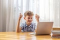 Excited schoolboy learning online on laptop