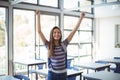 Excited schoolgirl standing with arms up in classroom