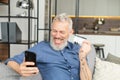 Excited senior bearded man wearing casual shirt looks at the phone screen surprised and happily Royalty Free Stock Photo