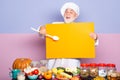 Excited senior chef in cook hat pointing spoon on blank board menu. Funny chef showing blank empty blackboard menu