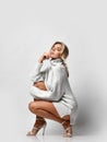 Sexy tall long-legged woman with closed eyes wearing knitted sweater on naked body and high-heeled shoes sits squatted