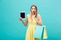 Excited shocked good-looking young woman in yellow dress while holding tablet and shopping bags. Royalty Free Stock Photo