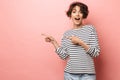 Excited shocked surprised beautiful woman posing isolated over pink wall background pointing