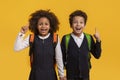 Excited siblings with school backpacks on yellow background