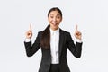 Excited smiling asian saleswoman in suit suggest great deal, pointing fingers up as telling details. Businesswoman