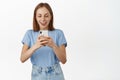 Excited smiling blond girl taking photo on mobile phone. Young happy woman looking amazed at smartphone screen, found Royalty Free Stock Photo