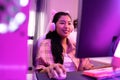 Excited and smiling gamer girl in cute headset with mic playing an online video game. Young Asian woman talking to Royalty Free Stock Photo