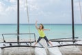 Excited smiling little girl standing on catamaran on tropical background