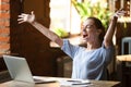 Excited smiling woman celebrating online win, using laptop in cafe