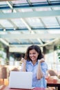 Excited smiling woman celebrating online win, using laptop in cafe, looking at screen, screaming with raising hands. Royalty Free Stock Photo