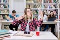 Excited smiling young girl in modern university library, sitting at the table and studying, making selfie on phone Royalty Free Stock Photo