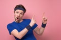 Excited sportive young man in blue t-shirt and hair band cheering and pointing on copyspace Royalty Free Stock Photo