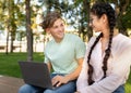 Excited students lady and guy studying together in park, preparing for exam and using laptop, sitting in park Royalty Free Stock Photo