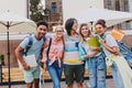 Excited students posing together in front of outdoor cafe, holding folders and laptops. Portrait of cheerful friends Royalty Free Stock Photo