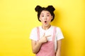 Excited stylish asian woman with glamour makeup, pointing finger right and gasping fascinated, say wow amazed, yellow Royalty Free Stock Photo