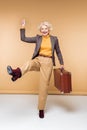 excited stylish senior female traveler with arm raised holding vintage