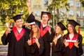 Excited successful five graduates in robes standing in row and showing certificate