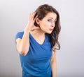 Excited surprising woman holding the hand near the ear and listening with emotional face the gossip on light grey background.