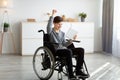 Excited teen boy in wheelchair holding tablet computer, celebrating his achievement or success, winning lottery at home