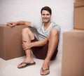 So excited to move into the new place. A happy young man sitting on the floor in his home amongst packed cardboard boxes